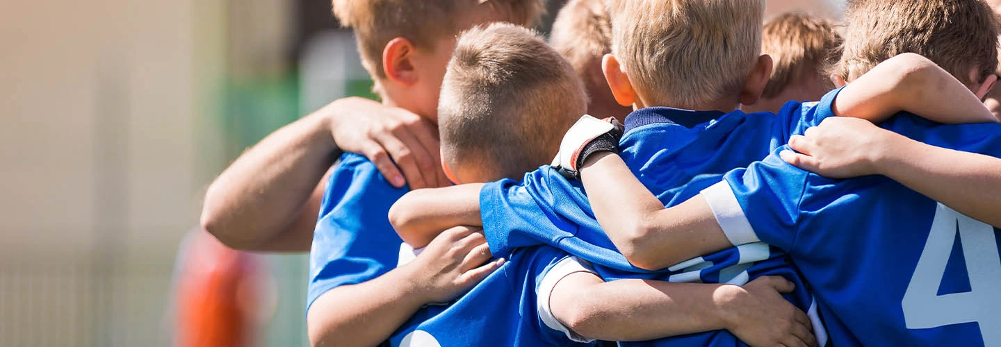 Kinder in blauen Trikots stehen mit den Armen umeinander in einer Teambesprechung