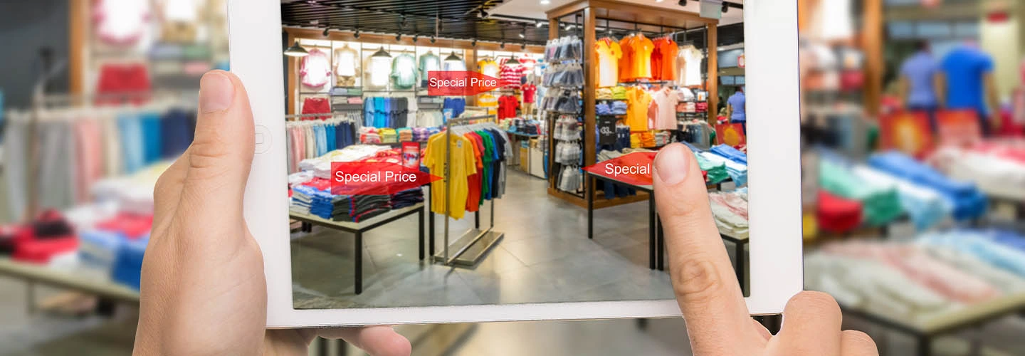 Hand hält ein Tablet mit einer Einkaufs-App vor Kleiderregalen in einem Geschäft